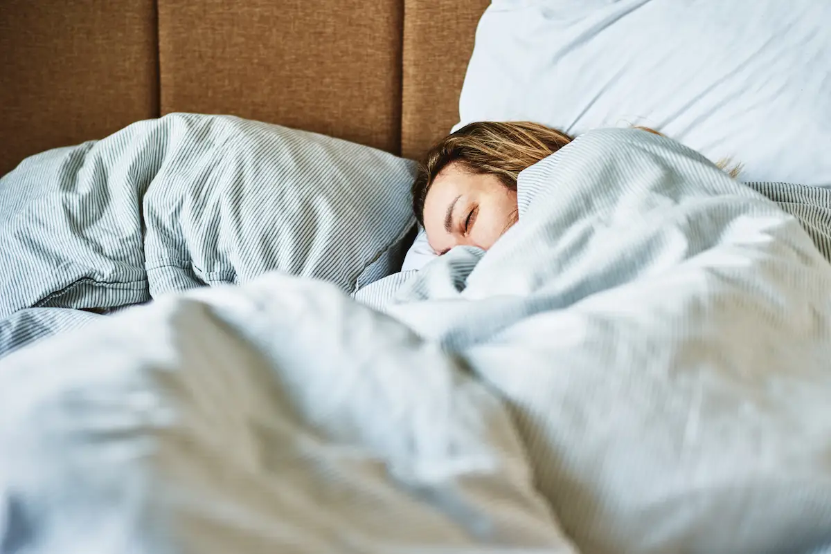Gesunder Schlaf: Frau schläft unter einer hellen Bettdecke